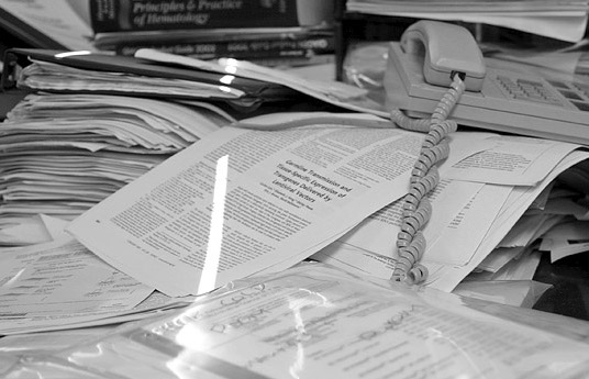 A pile of paperwork on a desk, with an old style phone and a stream of light artistically highlighting the paper.